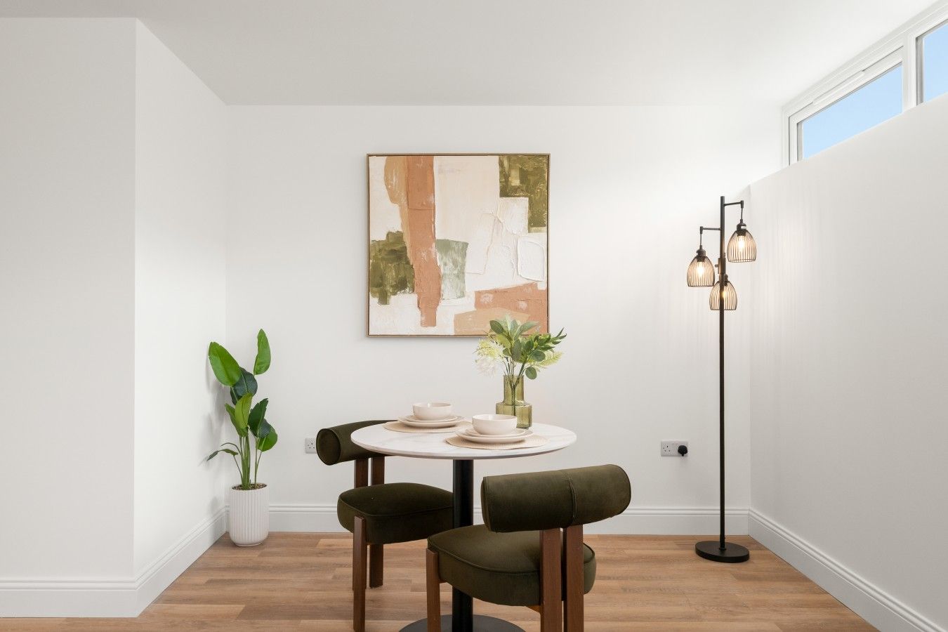Quarto com uma mesa redonda, duas cadeiras, um abajur e um quadro na parede.