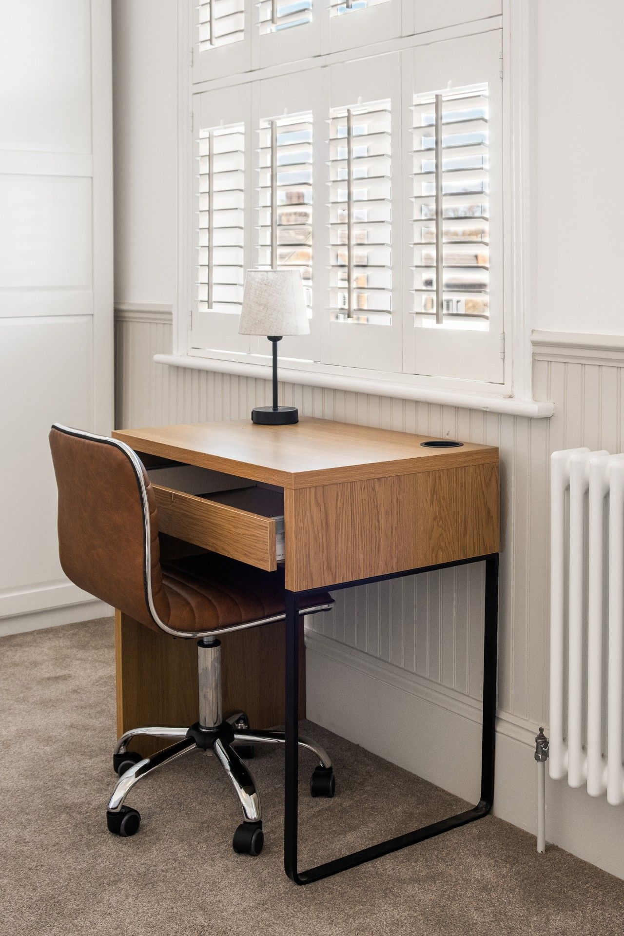 Un bureau en bois, une chaise, une lampe et une fenêtre avec des stores.