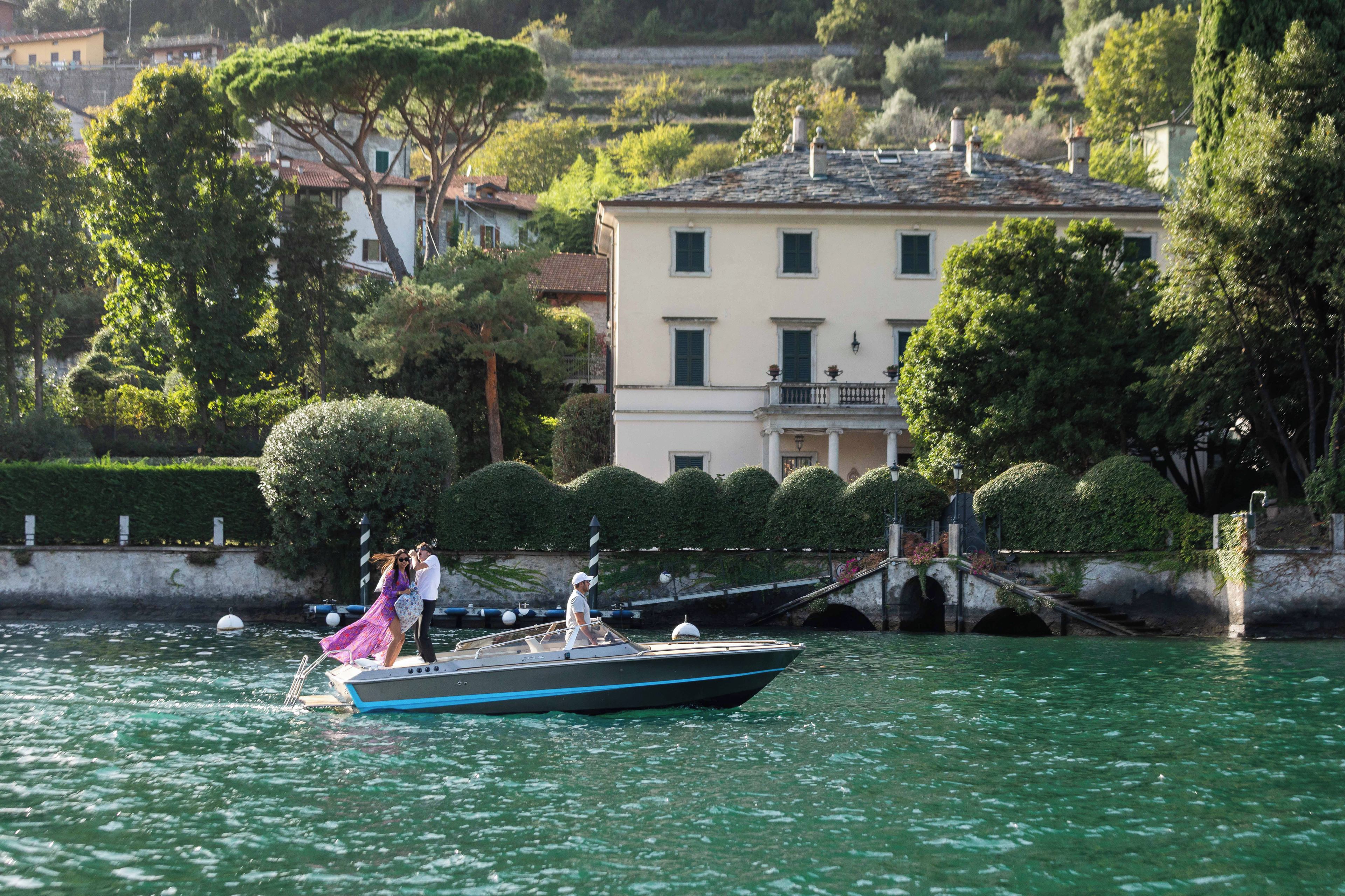 Un bateau sur une étendue d’eau calme, avec un bâtiment et des arbres en arrière-plan.