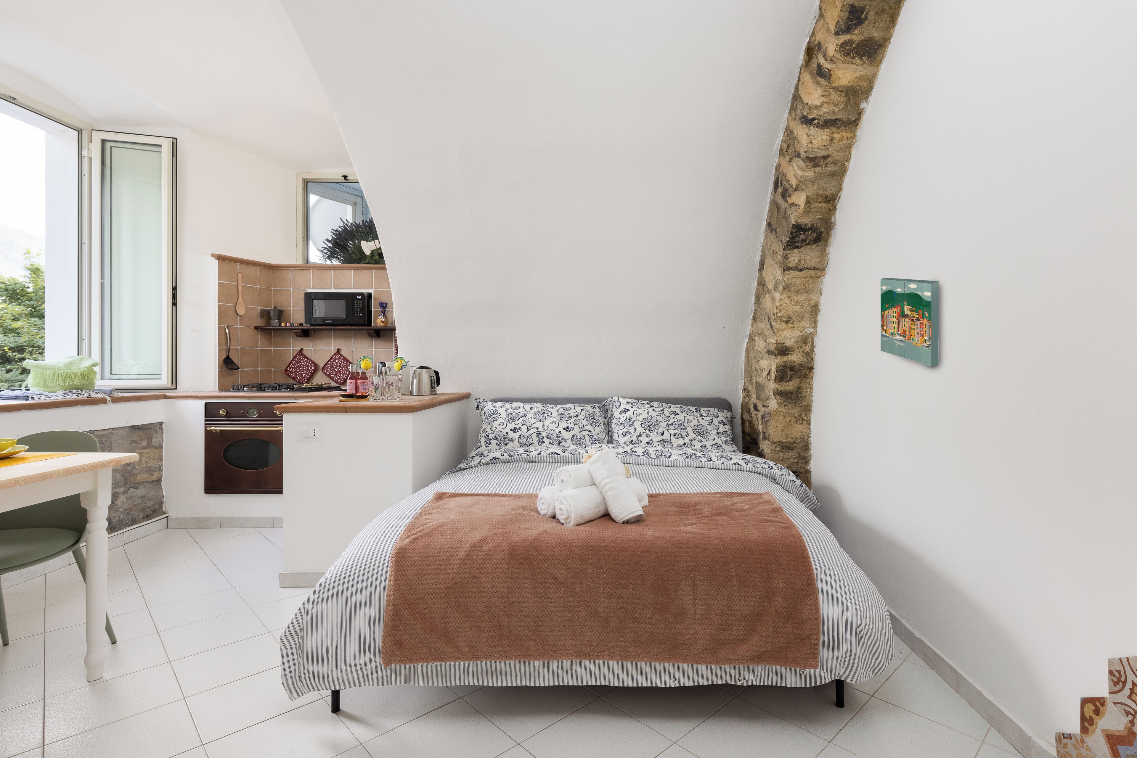 Ein Schlafzimmer mit Bett, Schreibtisch, einer Küchenzeile und Blick ins Freie.