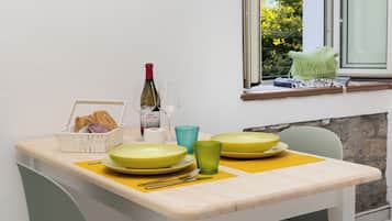 Une table à manger avec des sets de table jaunes, des assiettes vertes et jaunes, un panier de pain, une bouteille de vin et un verre d’eau.