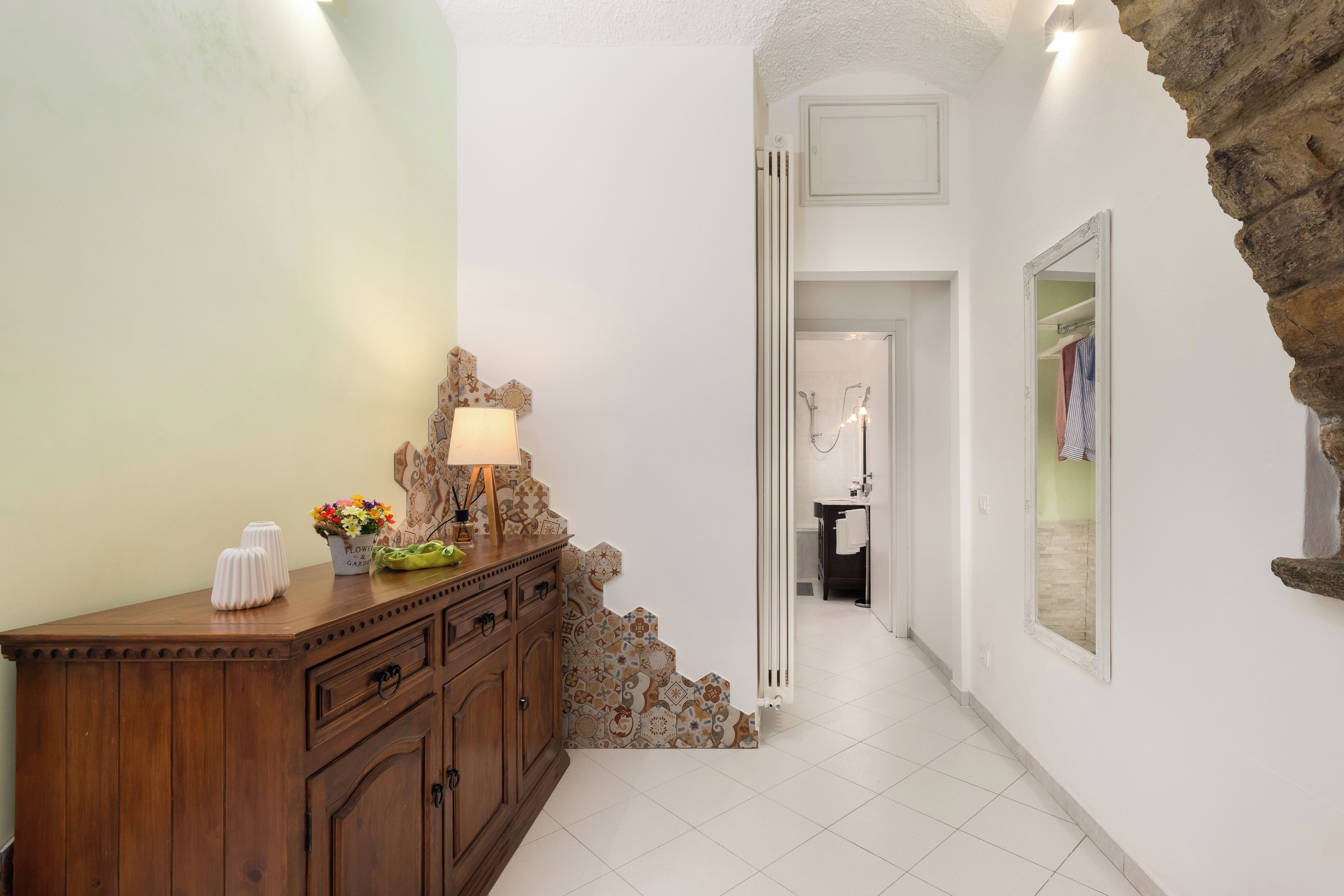 Un couloir avec une armoire en bois, une lampe et un vase à fleurs.