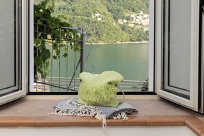 Ein Balkon mit Blick auf einen See und Hügel, einem Metallgeländer und einem grünen Kissen auf einer Wandteppich-Hängung.