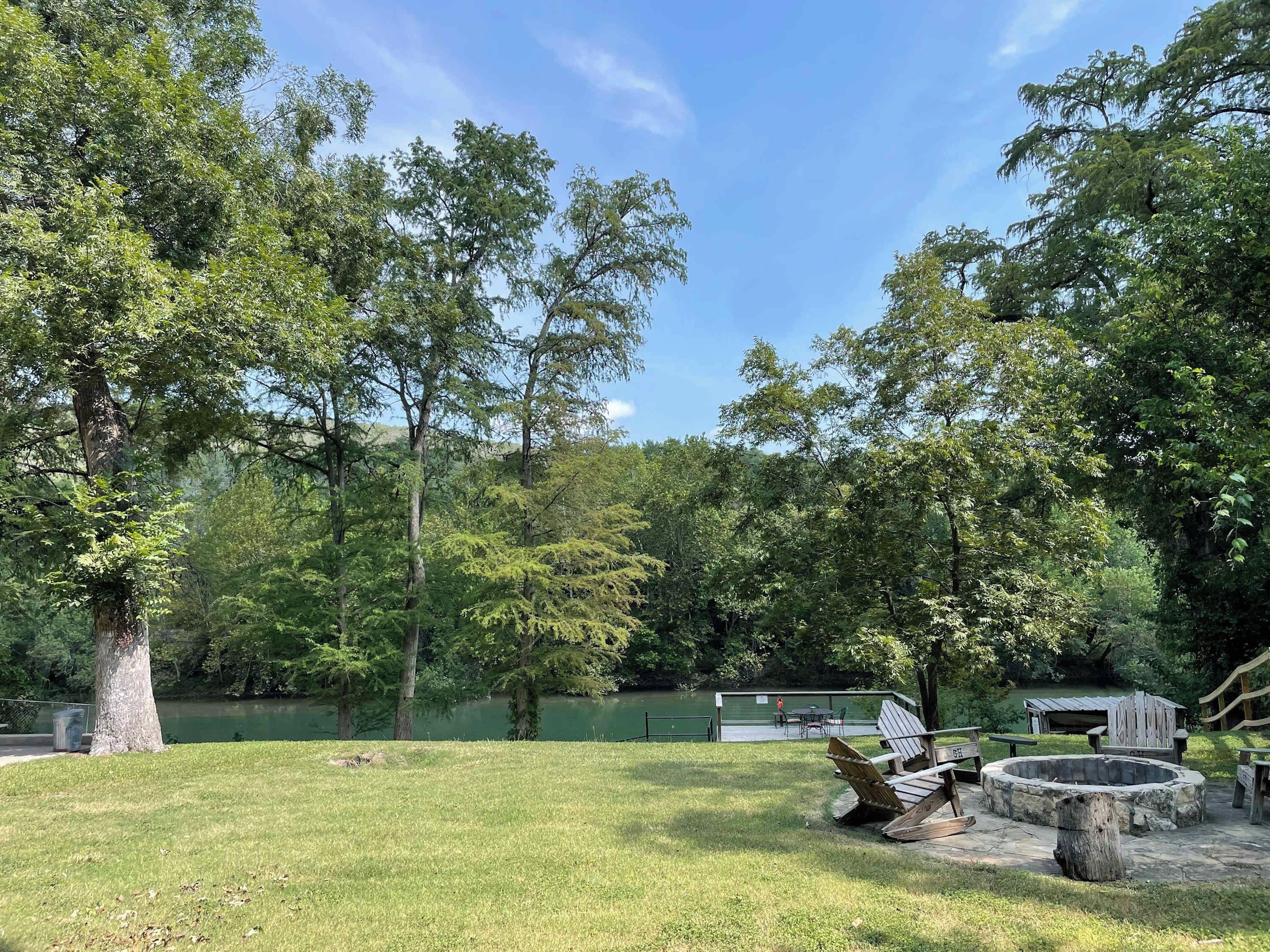 Un parc doté d’un foyer, de fauteuils Adirondack et d’une terrasse en bois offrant une vue sur un lac.