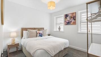 Un dormitorio con cama, mesita de noche, lámpara y ventana con persianas.