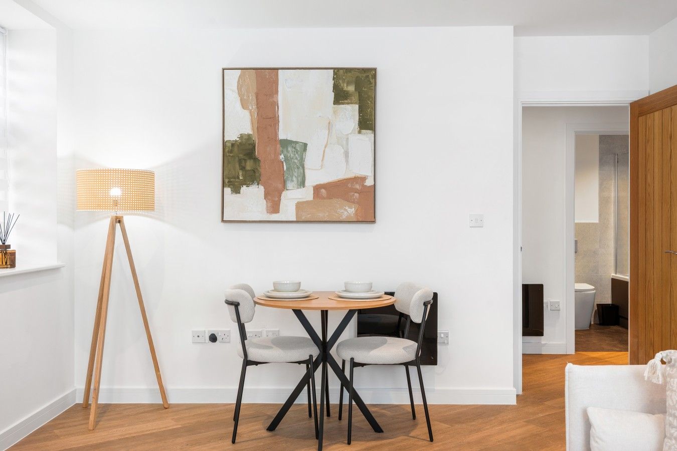 Un comedor moderno con una mesa redonda, dos sillas, una lámpara de pie y un cuadro en la pared.