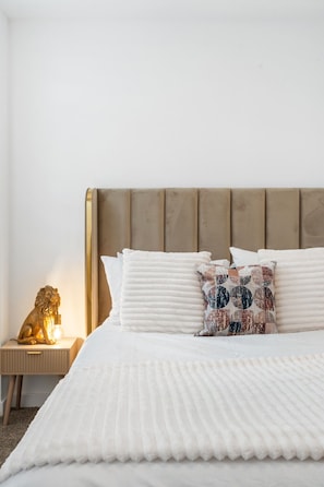 Una cama con colcha blanca, almohada estampada y cabecero de madera.