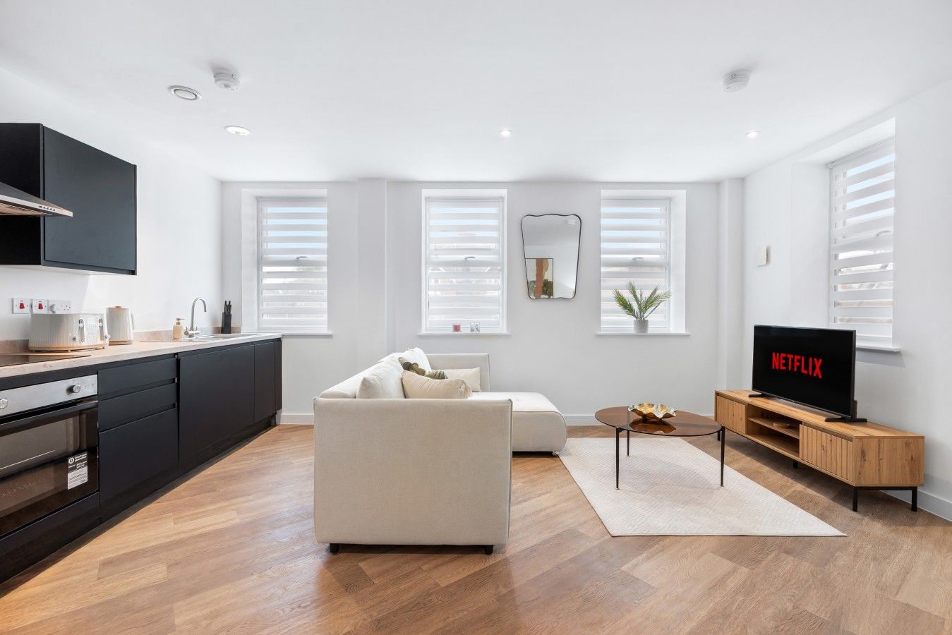Una sala de estar moderna con un sofá, un televisor y una zona de cocina con armarios y electrodomésticos.