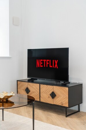 Un saló modern amb una televisió de pantalla plana sobre un moble negre, una taula de centre de vidre i un paviment de fusta.