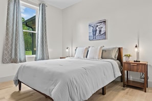 Ein Schlafzimmer mit einem großen Bett, einem Nachttisch mit Lampe und einem Fenster mit Vorhängen.