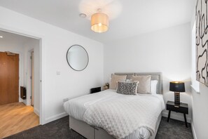Un dormitorio con una cama, mesitas de noche, una lámpara, un espejo y una puerta.