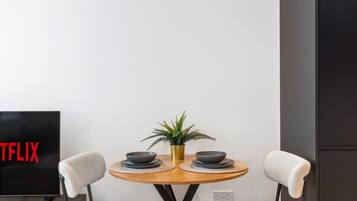 Un comedor moderno con una mesa redonda, dos sillas, una planta en maceta y un televisor que muestra el logotipo de Netflix.