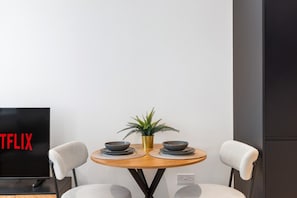 Un comedor moderno con una mesa redonda, dos sillas, una planta en maceta y un televisor que muestra el logotipo de Netflix.