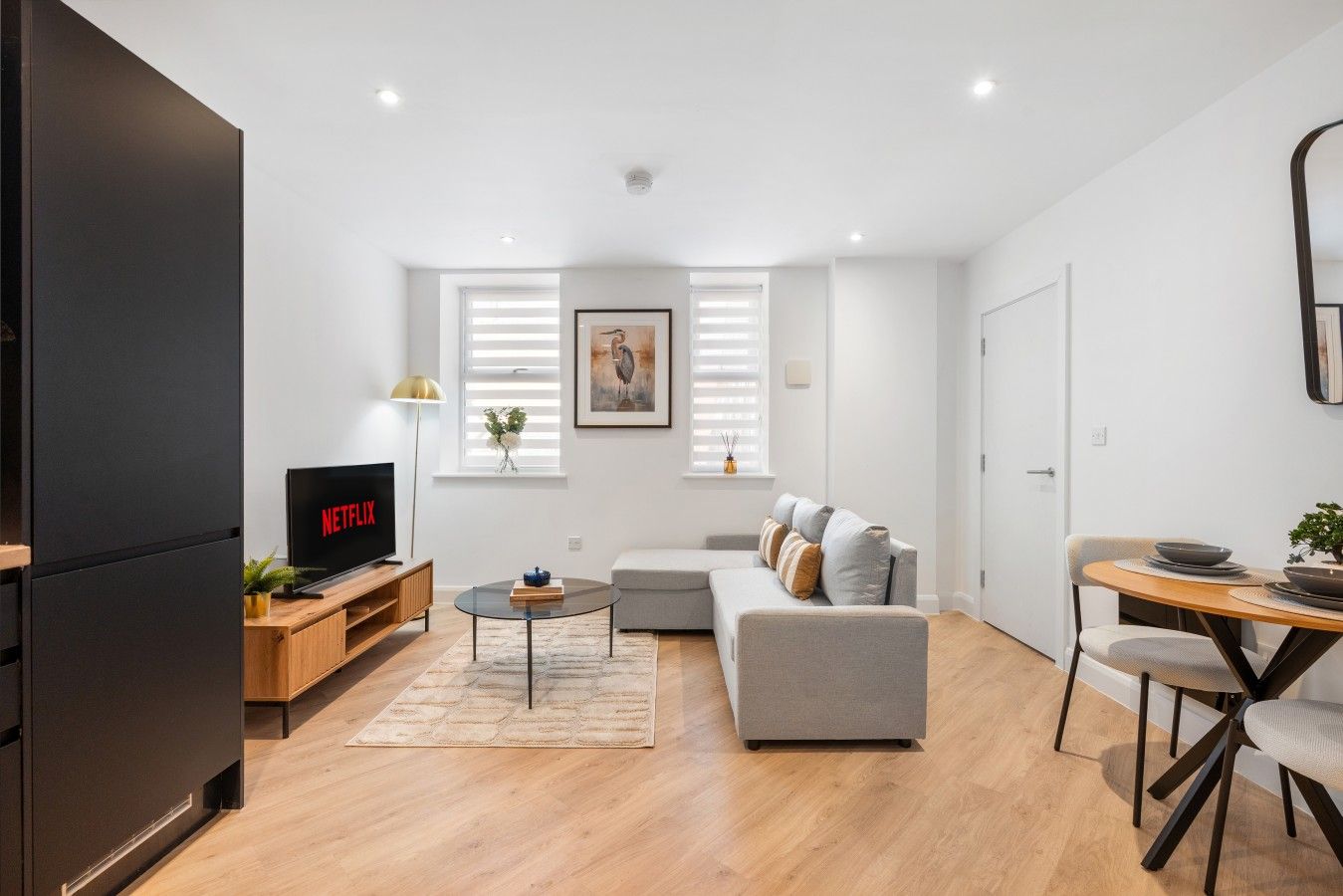 Una sala de estar moderna con un televisor de pantalla plana, un sofá, una mesa de comedor con sillas y una zona de cocina con refrigerador.