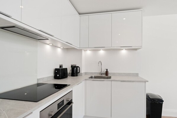 A modern kitchen with white cabinetry, a built-in oven, a stovetop, and a coffee maker. - Bluewater Retreat | 2 BR | Sleeps 3 | Free Parking (Kent)