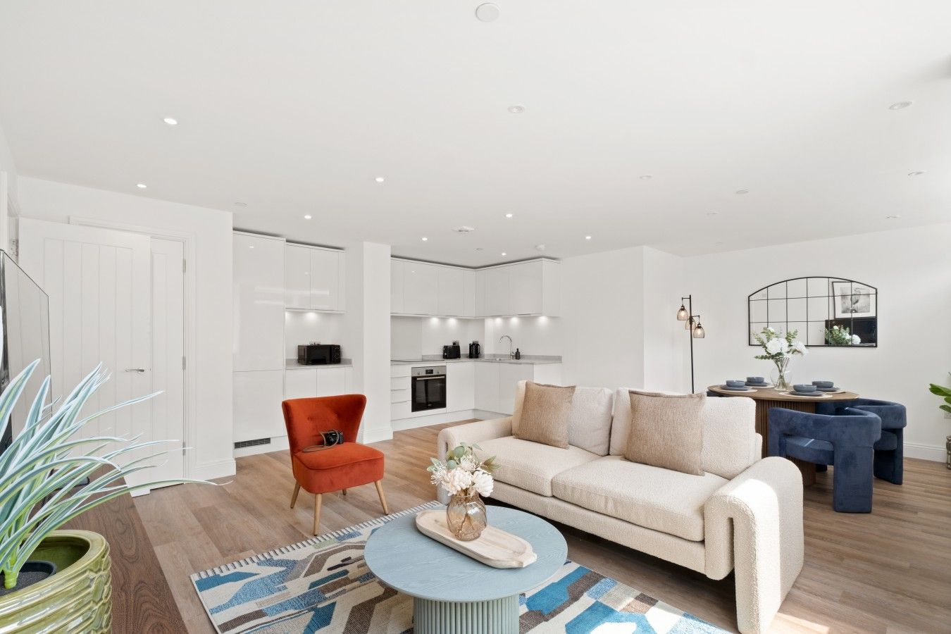 Uma sala de estar moderna com um sofá, uma poltrona vermelha e uma área de jantar com mesa e cadeiras.