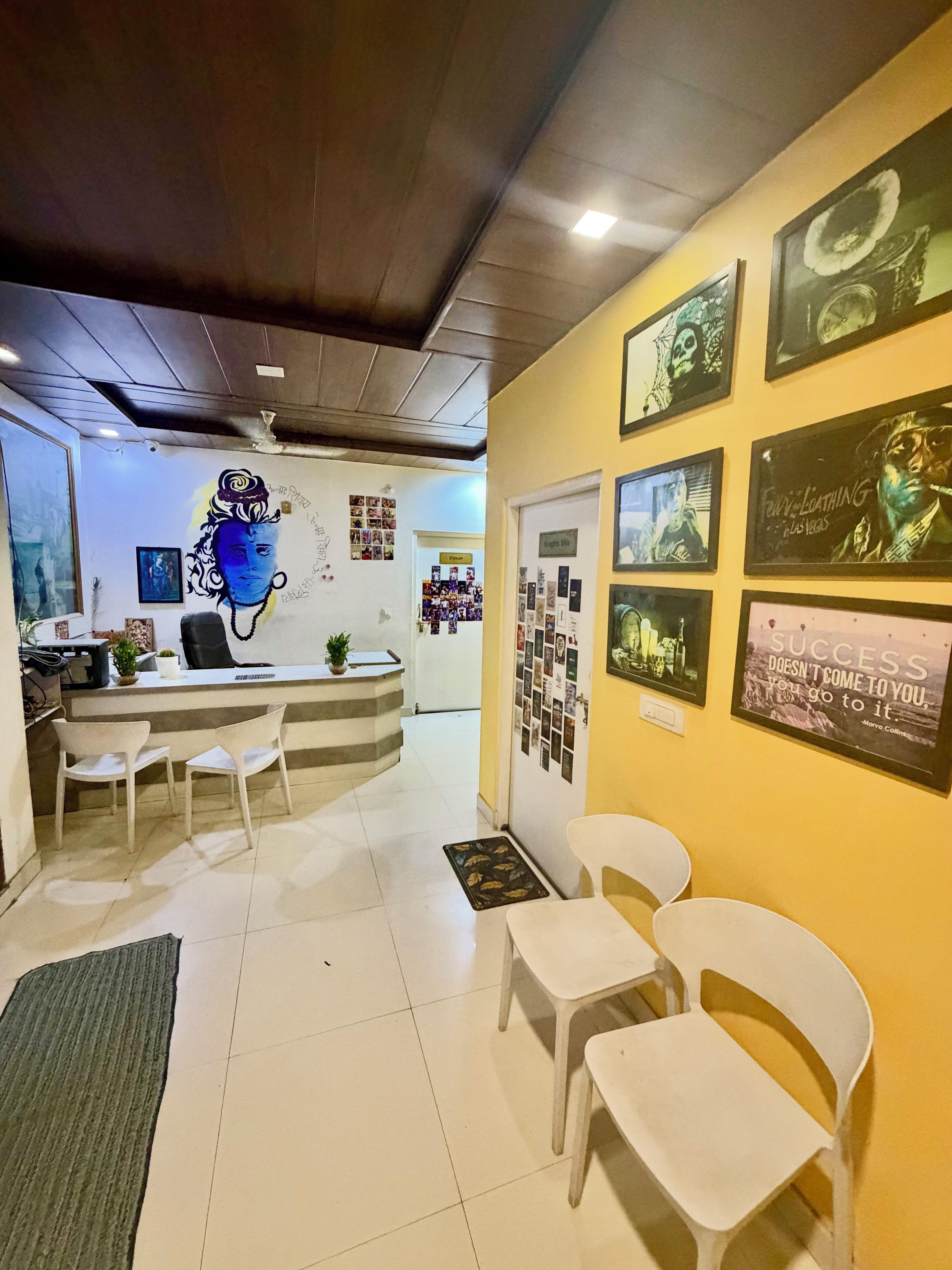 Un'area di accoglienza con un banco reception, sedie e una parete decorata con quadri incorniciati e un murale.