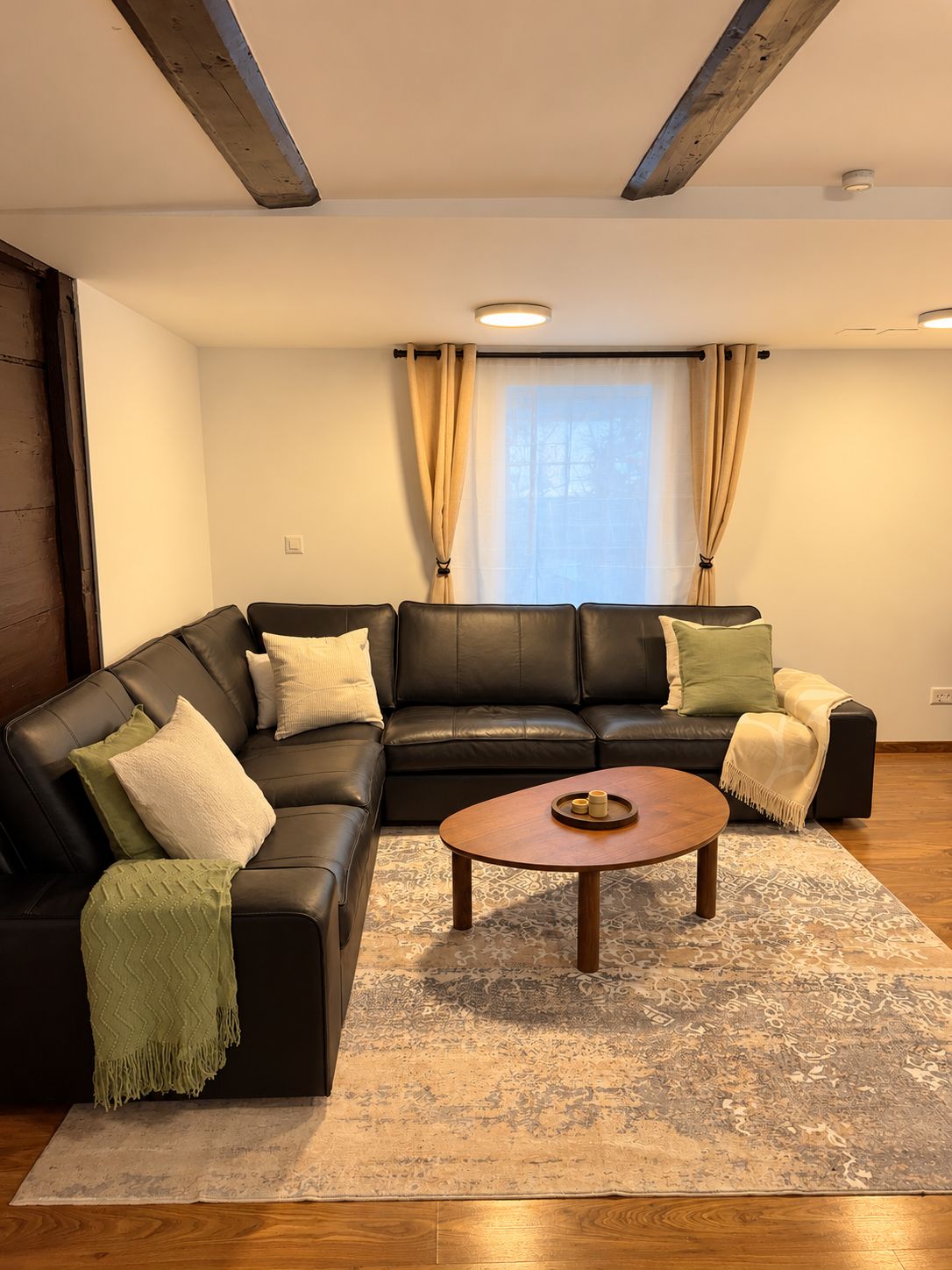 A living room with a black leather sofa, a wooden coffee table, and patterned rugs.