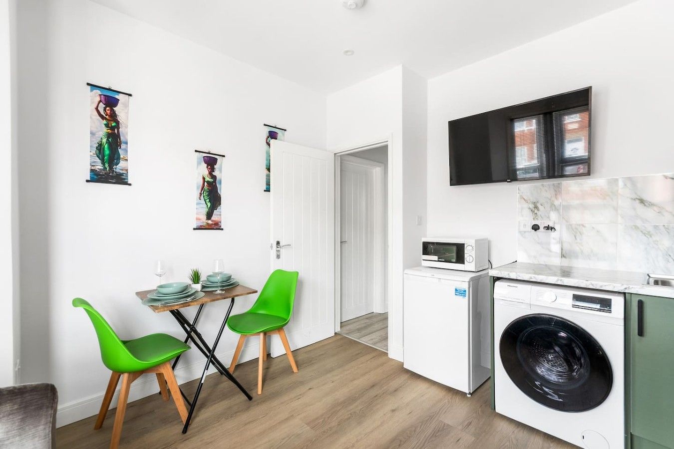 A modern kitchen with a washing machine, a microwave, and a flat-screen TV.