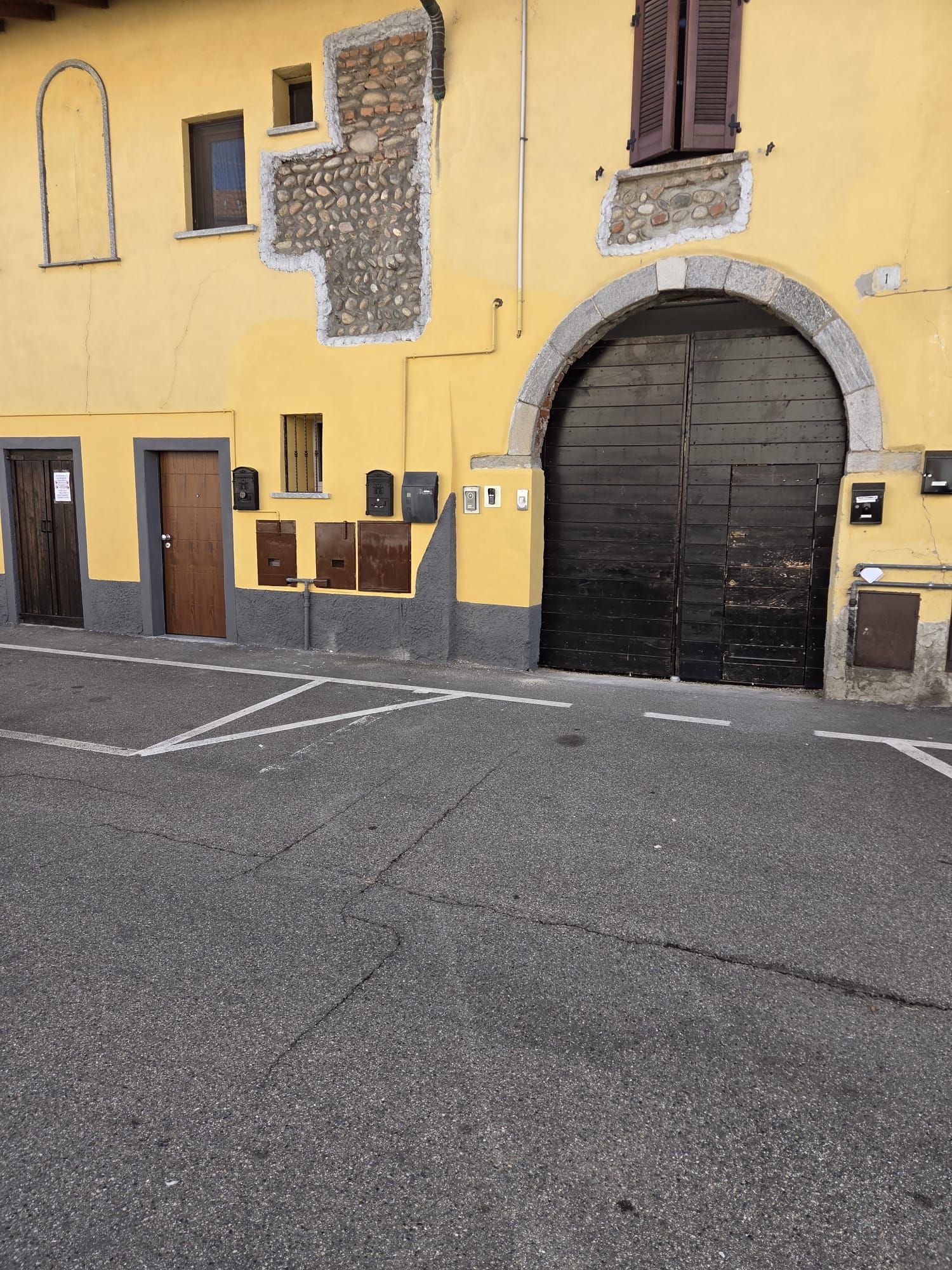 Un bâtiment jaune avec un grand portail noir, une petite fenêtre et une porte.