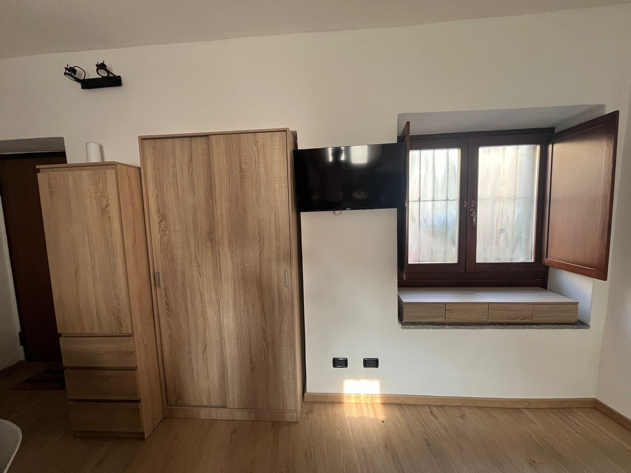 Ein Zimmer mit einem Holzschrank, einem flachbildfernseher an der Wand und einem Fenster mit Blick.