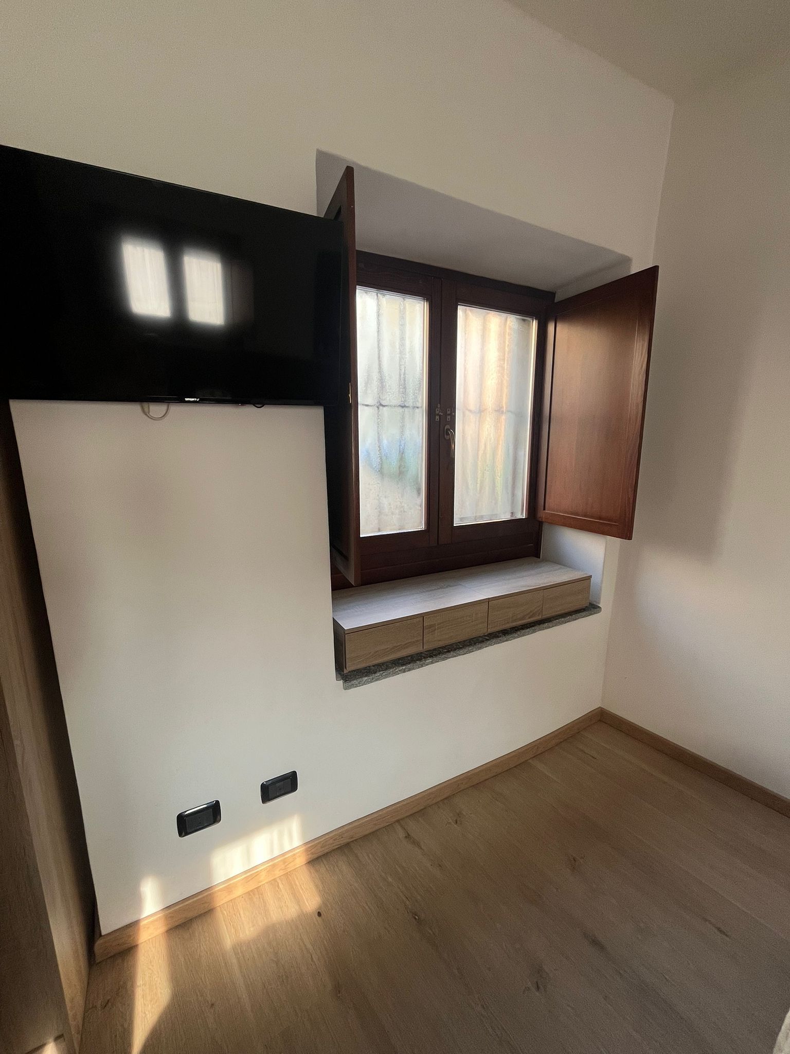 A room with a built-in window, a flat-screen TV, and a wooden floor.