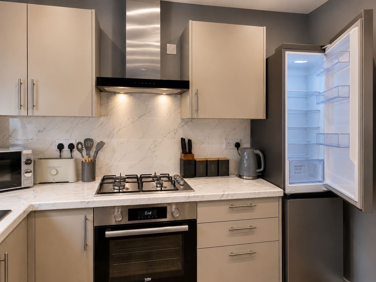A modern kitchen with a built-in microwave, toaster, gas stove, oven, and a refrigerator with a humidity control feature.