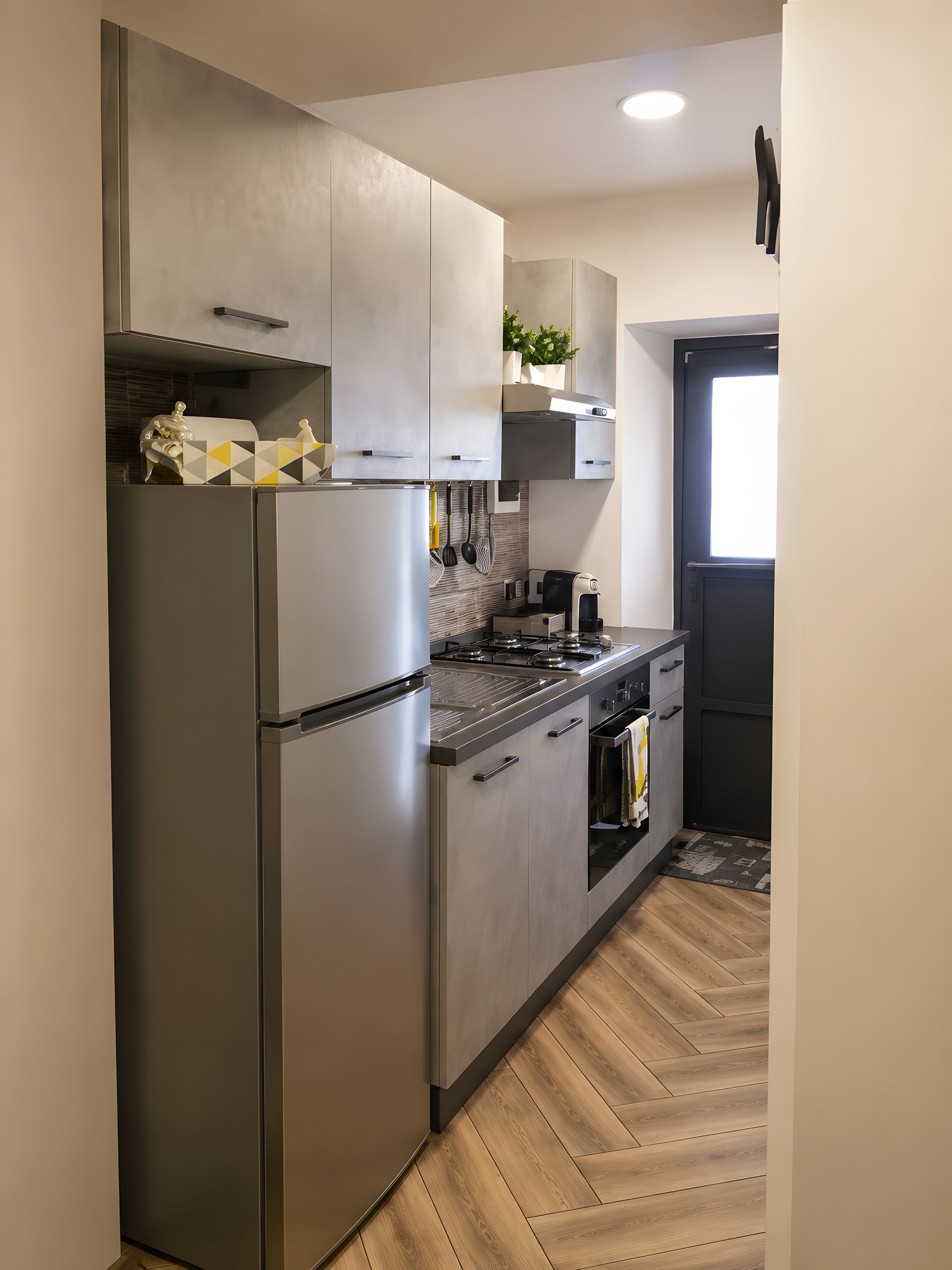 Una cocina moderna con electrodomésticos de acero inoxidable, suelo de madera y una puerta negra.