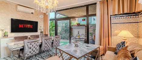 A living room with a TV, seating, a chandelier, and a view of the outdoors.