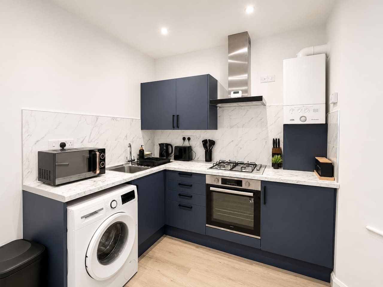 A compact kitchen with a washing machine, microwave, stove, and cabinets.