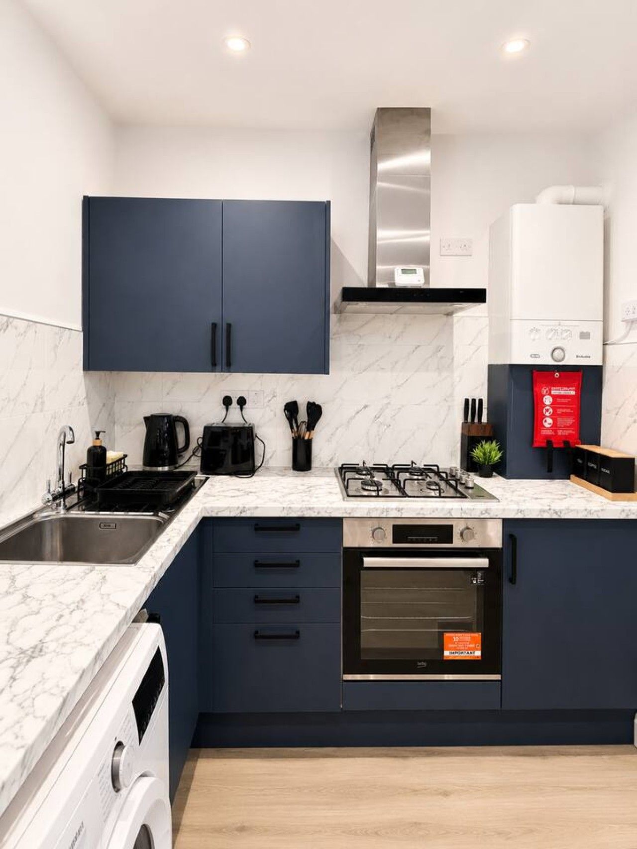 A modern kitchen with dark blue cabinets, a stainless steel sink, a gas stove, and a built-in oven.