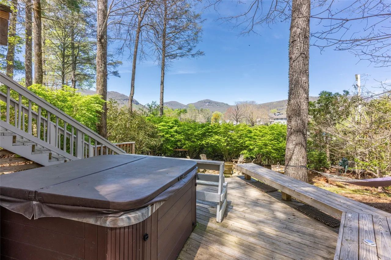 Una terraza de madera con un jacuzzi, una escalera de madera y vistas a una zona boscosa con colinas al fondo.
