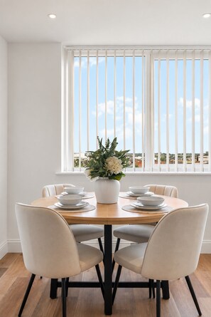Uma sala de jantar com uma mesa redonda, cadeiras brancas e um vaso de flores.