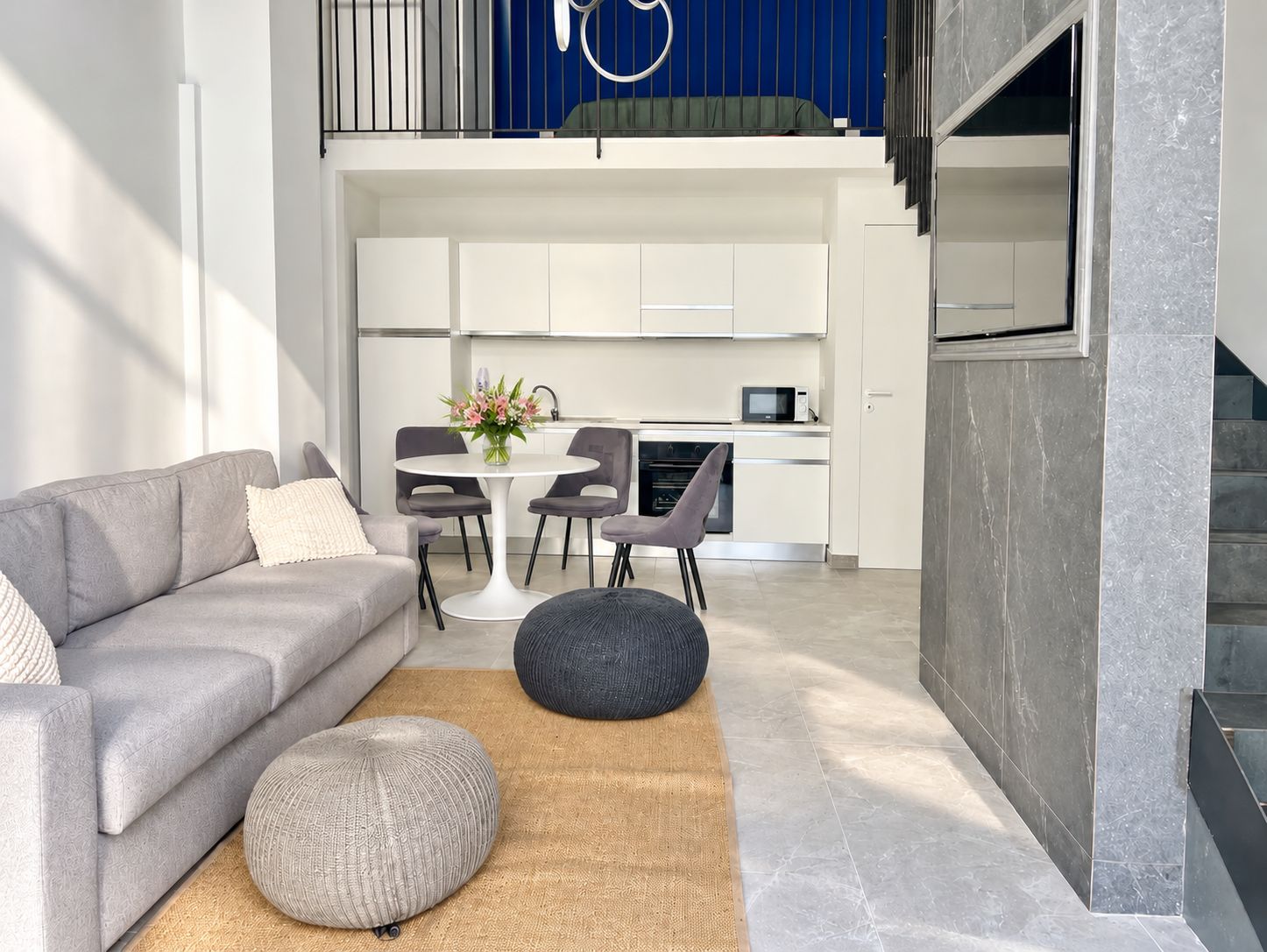 Un espacio de estar moderno con sofá, reposapiés y zona de comedor con sillas y mesa.