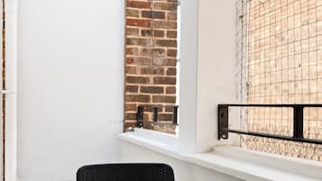 A balcony with two chairs and a table, a white wall, a brick wall, and a window with a metal grille.
