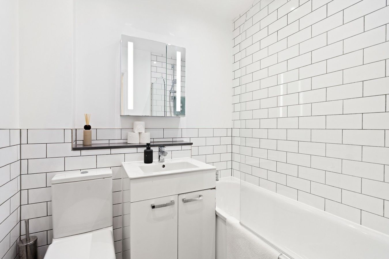 A modern bathroom with white tiles, a sink, a mirror, and a bathtub.
