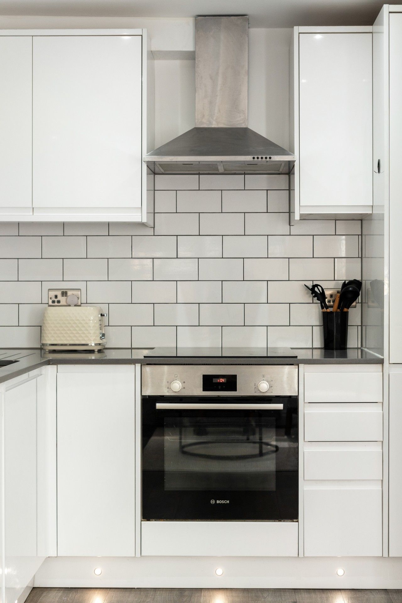 A kitchen with white cabinets, a Bosch oven, and a tiled backsplash.