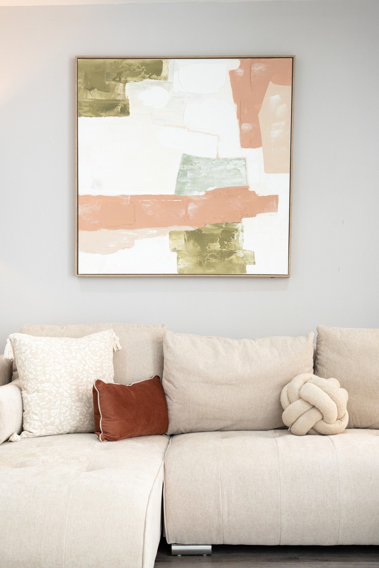 A living room with a beige sofa, a decorative throw pillow, and a framed abstract painting on the wall.