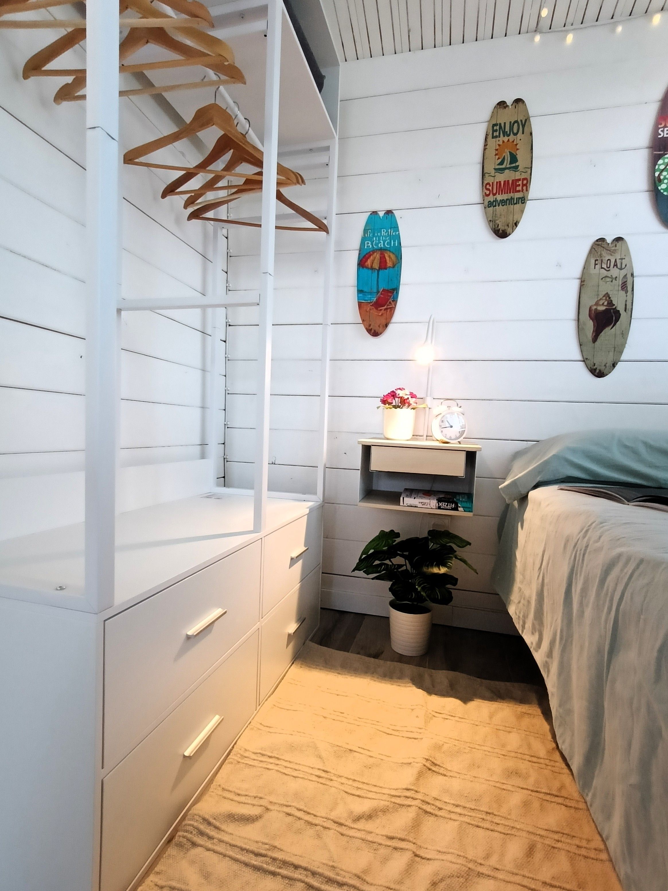 Ein Schlafzimmer mit einem Bett, einem Nachttisch mit einer Uhr, einem an der Wand befestigten Regal mit Dekoration und einem Holzschrank.