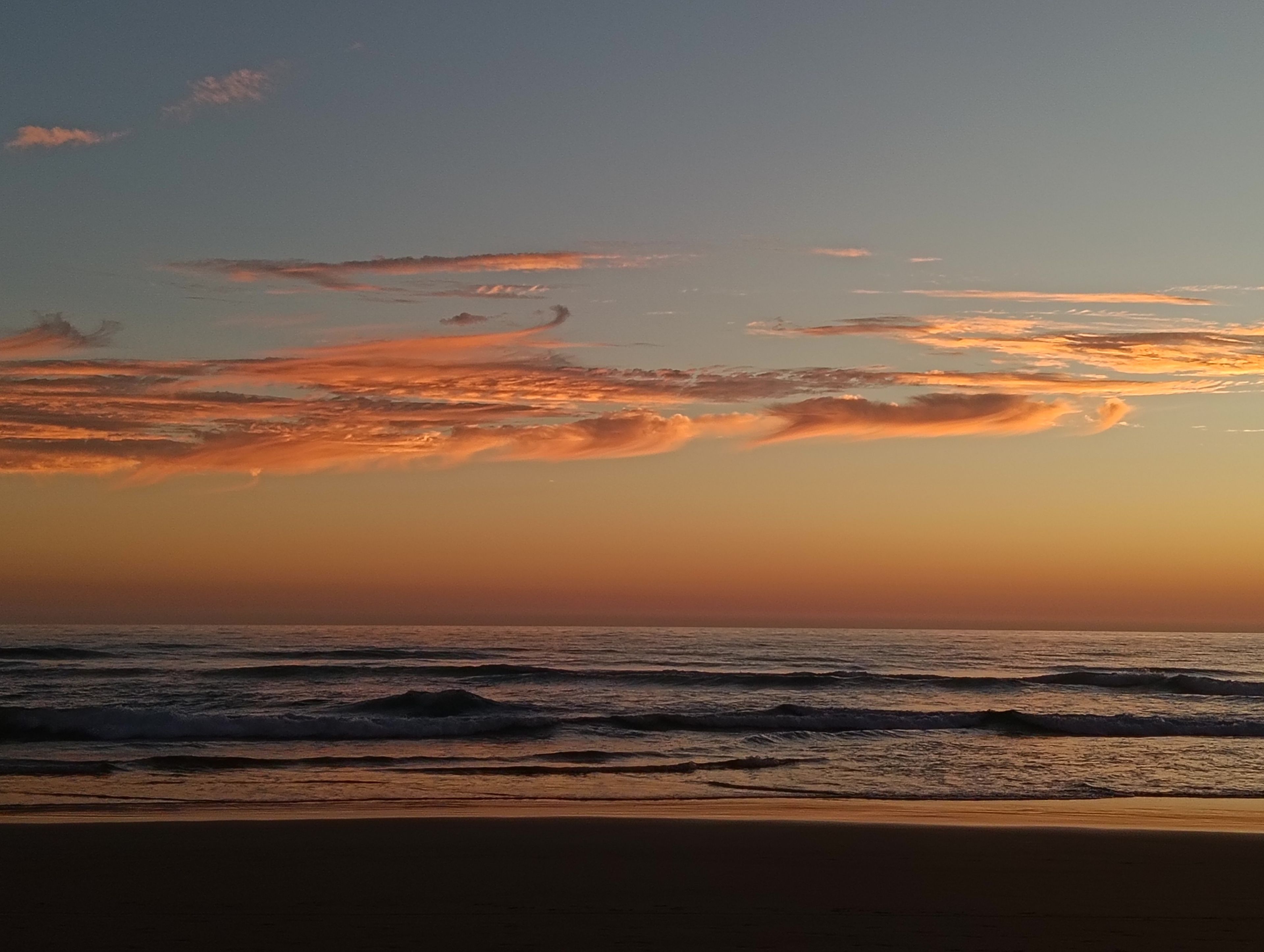 A beach with waves and a sunset sky.