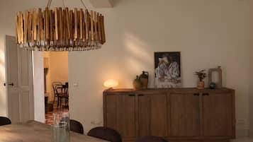 Un comedor con una mesa de madera larga, sillas, una lámpara colgante de madera y un aparador de madera con adornos.