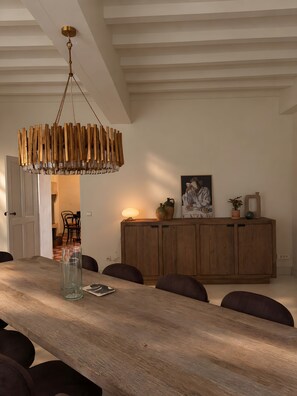 Un comedor con una mesa de madera larga, sillas, una lámpara colgante de madera y un aparador de madera con adornos.