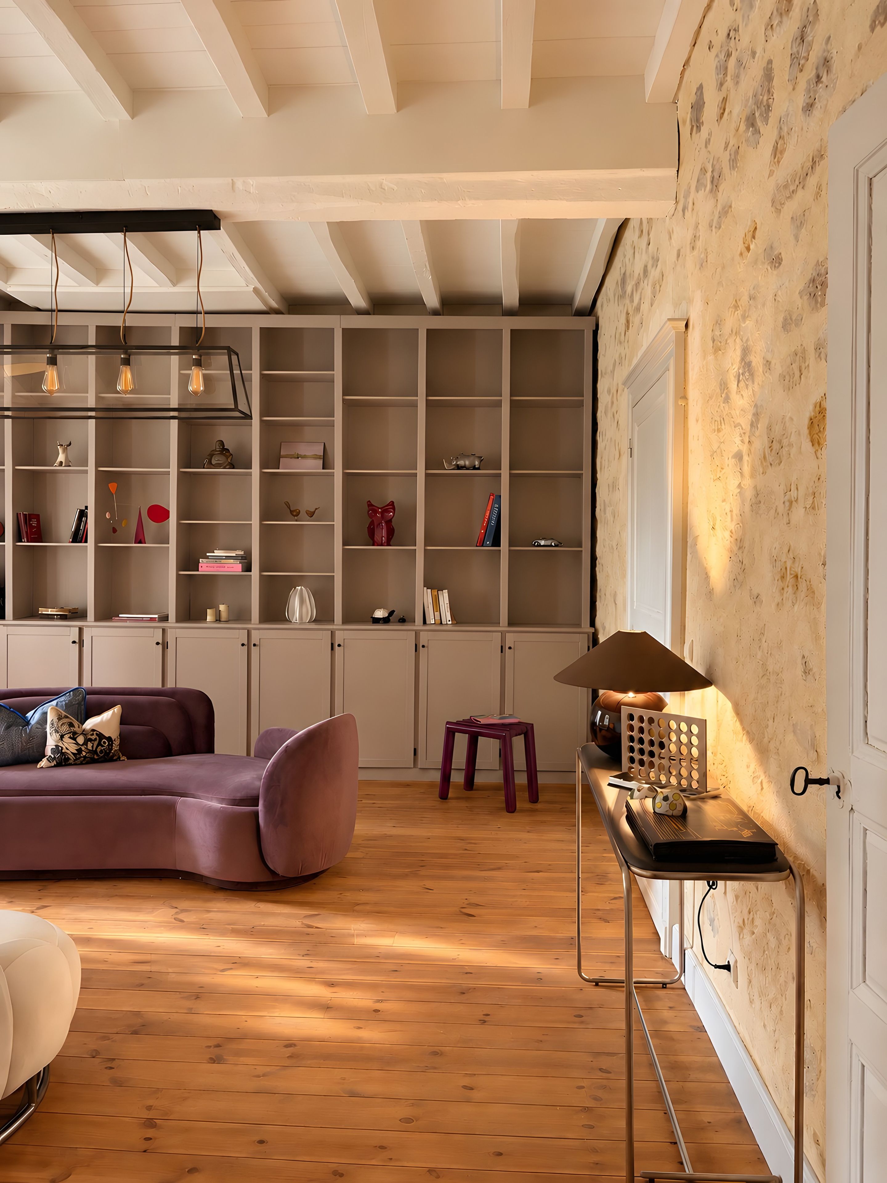 A modern living room with a wooden floor, a purple sofa, a small stool, and a table with a lamp.