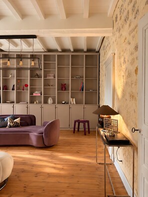 Ein modernes Wohnzimmer mit Holzboden, einem violetten Sofa, einem kleinen Hocker und einem Tisch mit einer Lampe.