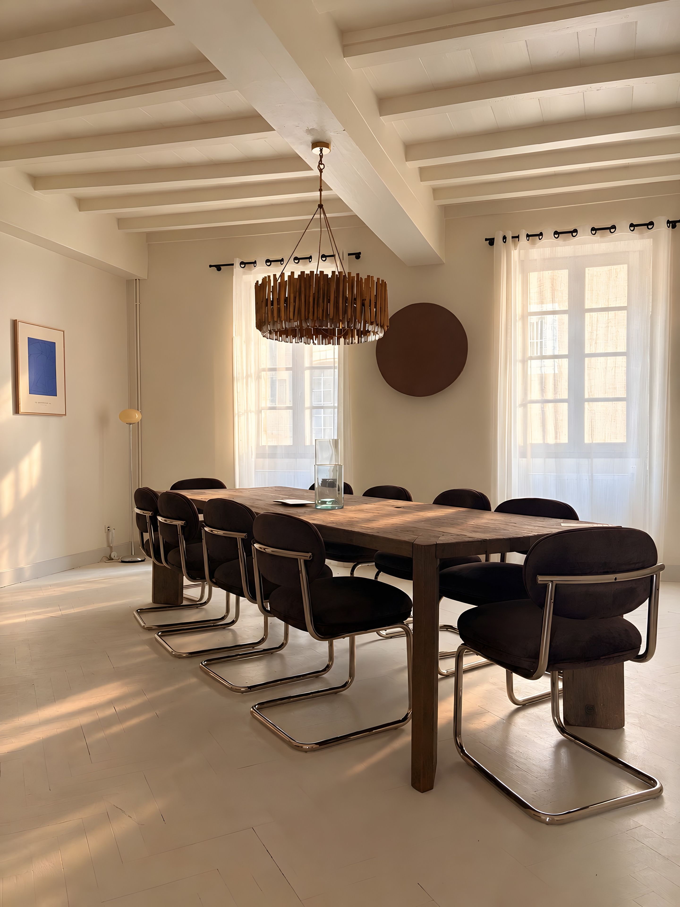 Un comedor con mesa de madera, sillas negras, lámpara colgante y ventanas amplias.