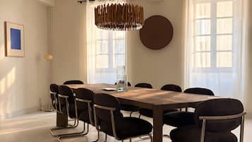 Un comedor con mesa de madera, sillas negras, lámpara colgante y ventanas amplias.
