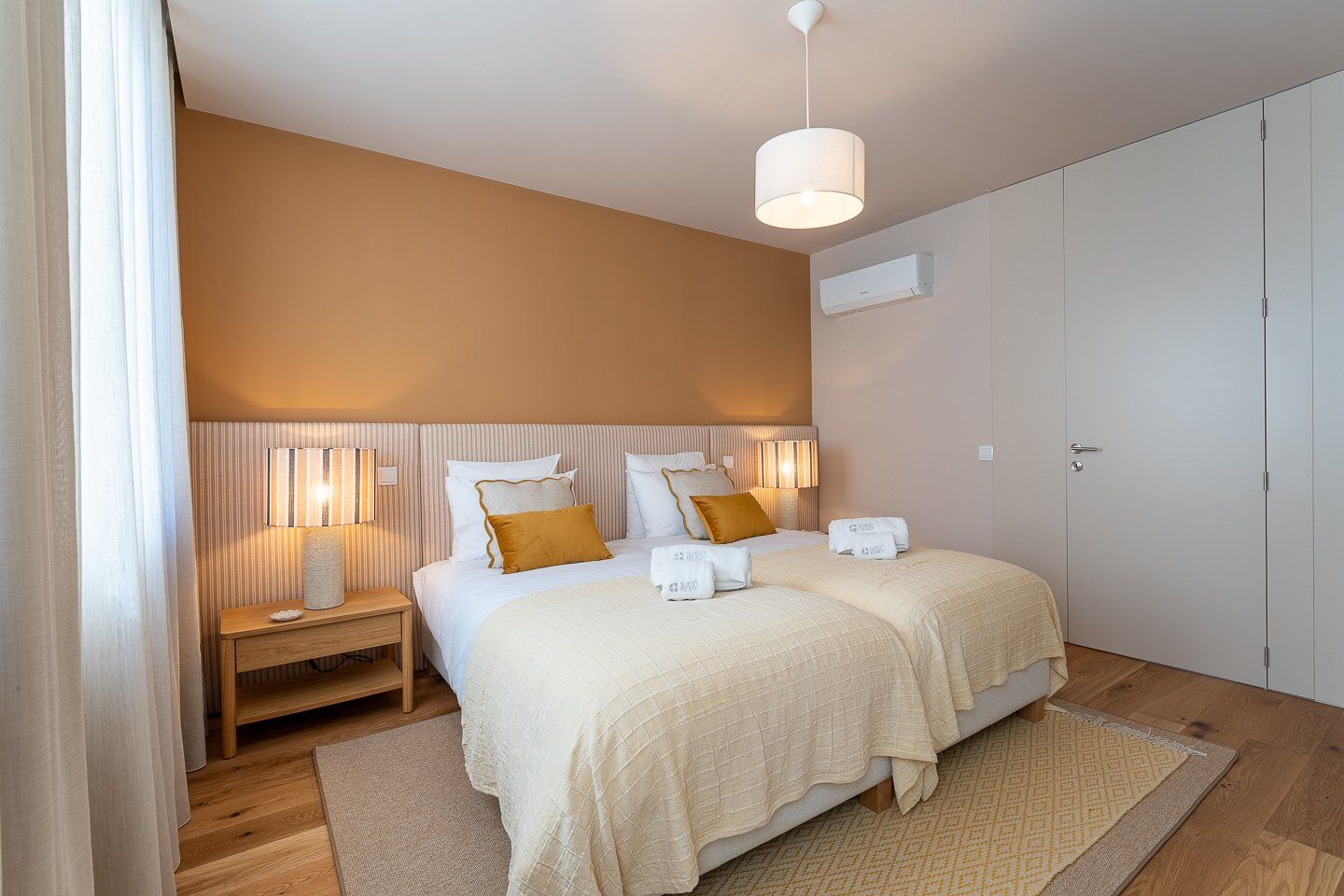A hotel room with a bed, bedside lamps, a nightstand, a wardrobe, and a hanging light fixture.