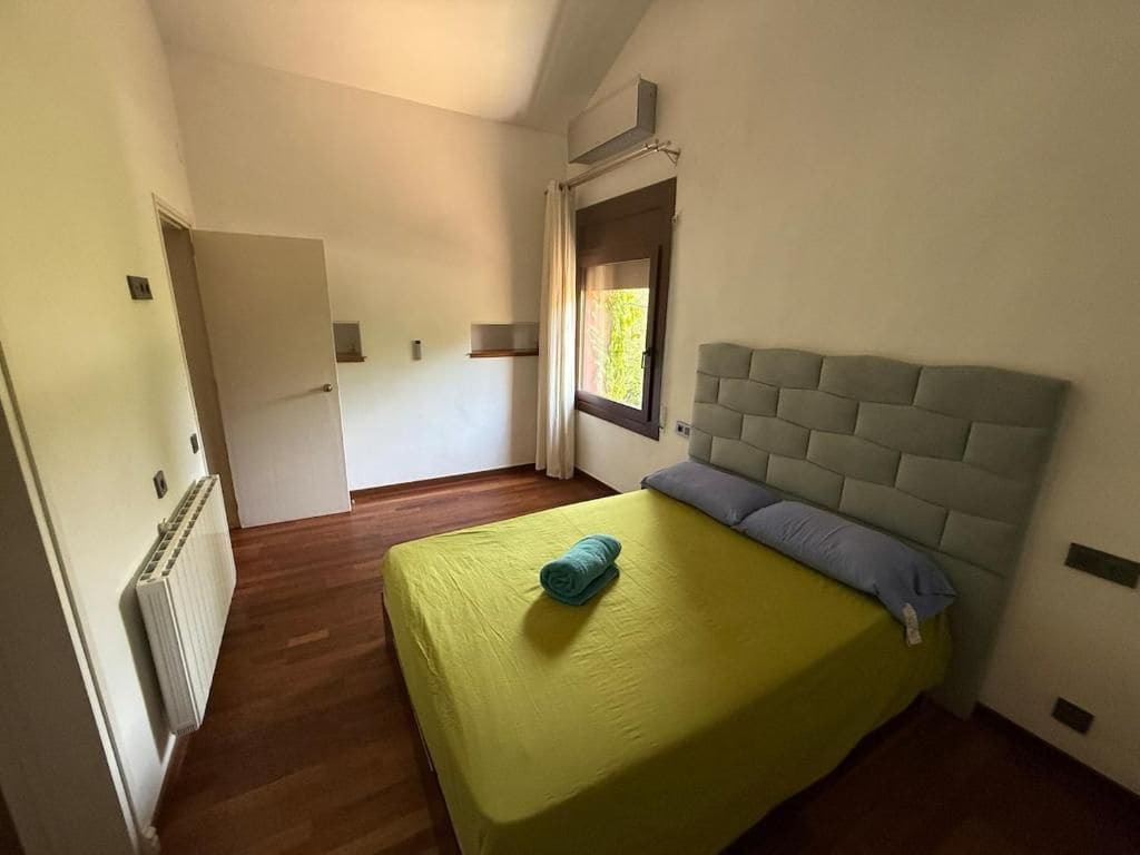 Ein Schlafzimmer mit einem Bett, einem Heizkörper, einem Fenster mit Vorhängen und einer Tür zu einem anderen Raum.