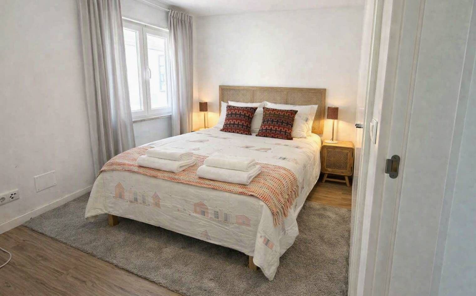 A bedroom with a bed, a bedside table, a lamp, and a window with curtains.