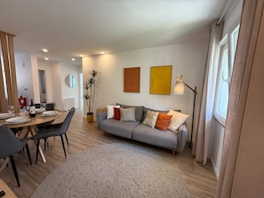 A modern living room with a grey sofa, a dining table with chairs, a floor lamp, and a potted plant. - Charming Apartment near Parede Beach (Cascais)